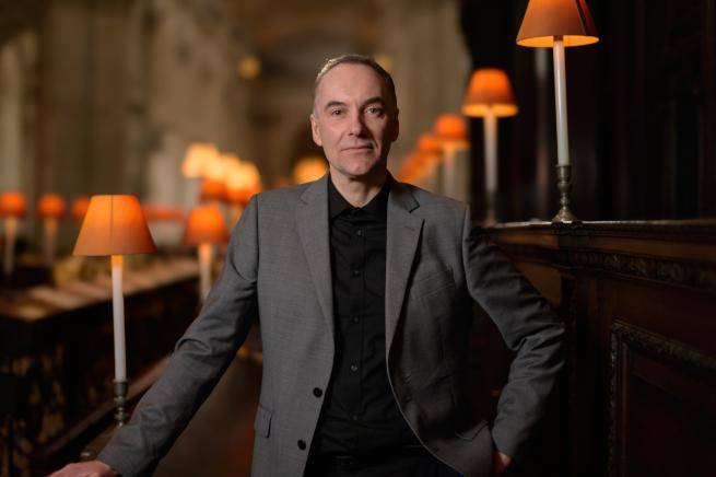 An image of a white man with cropped hair and grey suit jacket standing in front of choir stalls inside St Paul's Cathedral