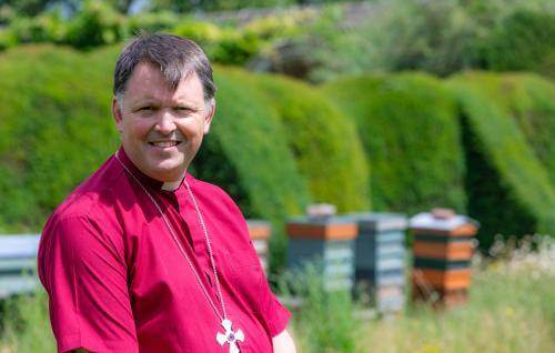 Graham Usher in a garden with beehives in the background