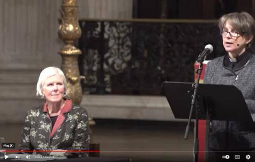 Lucy Winkett speaking from the lectern at St Paul's Cathedral with Marian Partington listening from a table beside her.