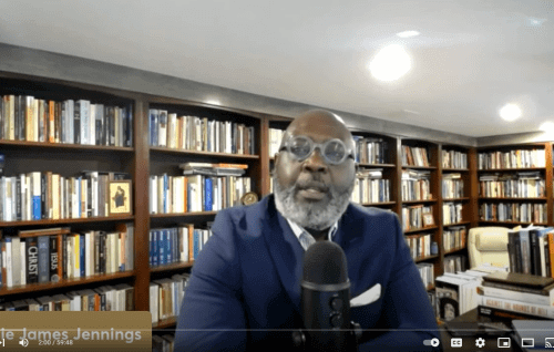 Willie Jennings on screen during the lecture in his office with rows of bookcases behind