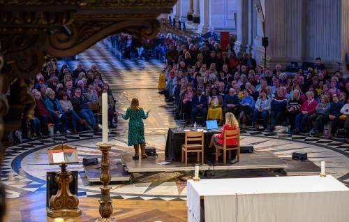 A view of the cathedral with a large audience facing a stage with a speaker in a green dress