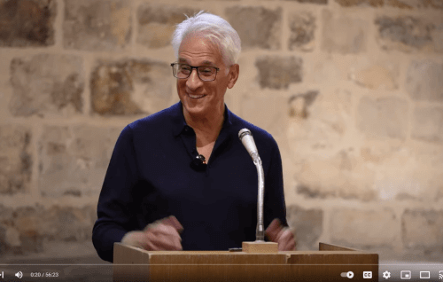 Steve is a mixed race man with white hair and black glasses, talking at a microphone in the Wren Suite at St Paul's Cathedral