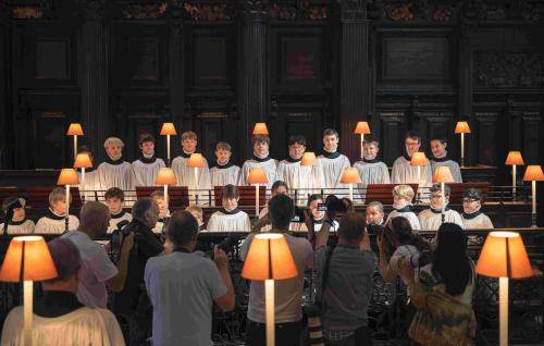 St Paul's Cathedral choristers stand in the Cathedral quire, which is lit with lamps. They are stood in two rows, and are being photographed by a group of press photographers.